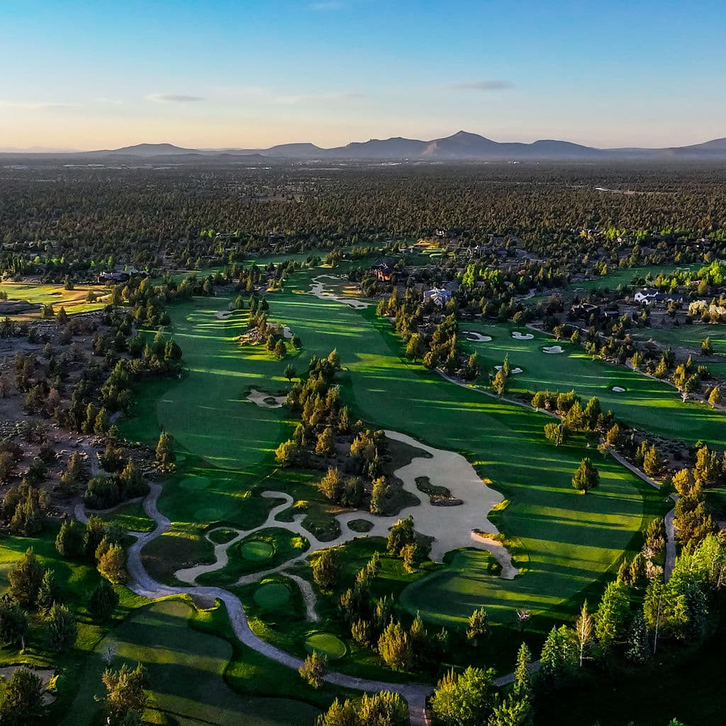 Pronghorn from the air at golden hour: fairways and white bunkers winding through juniper, with mountains on the horizon.